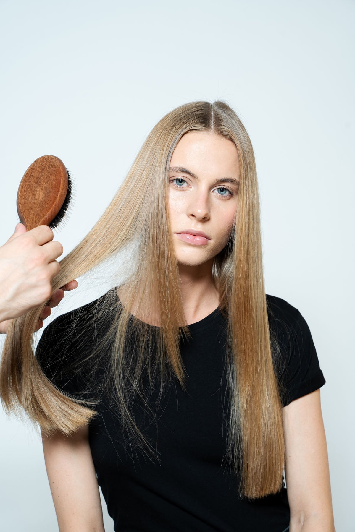 Woman with long blonde hair being styled with a wooden brush against a white background