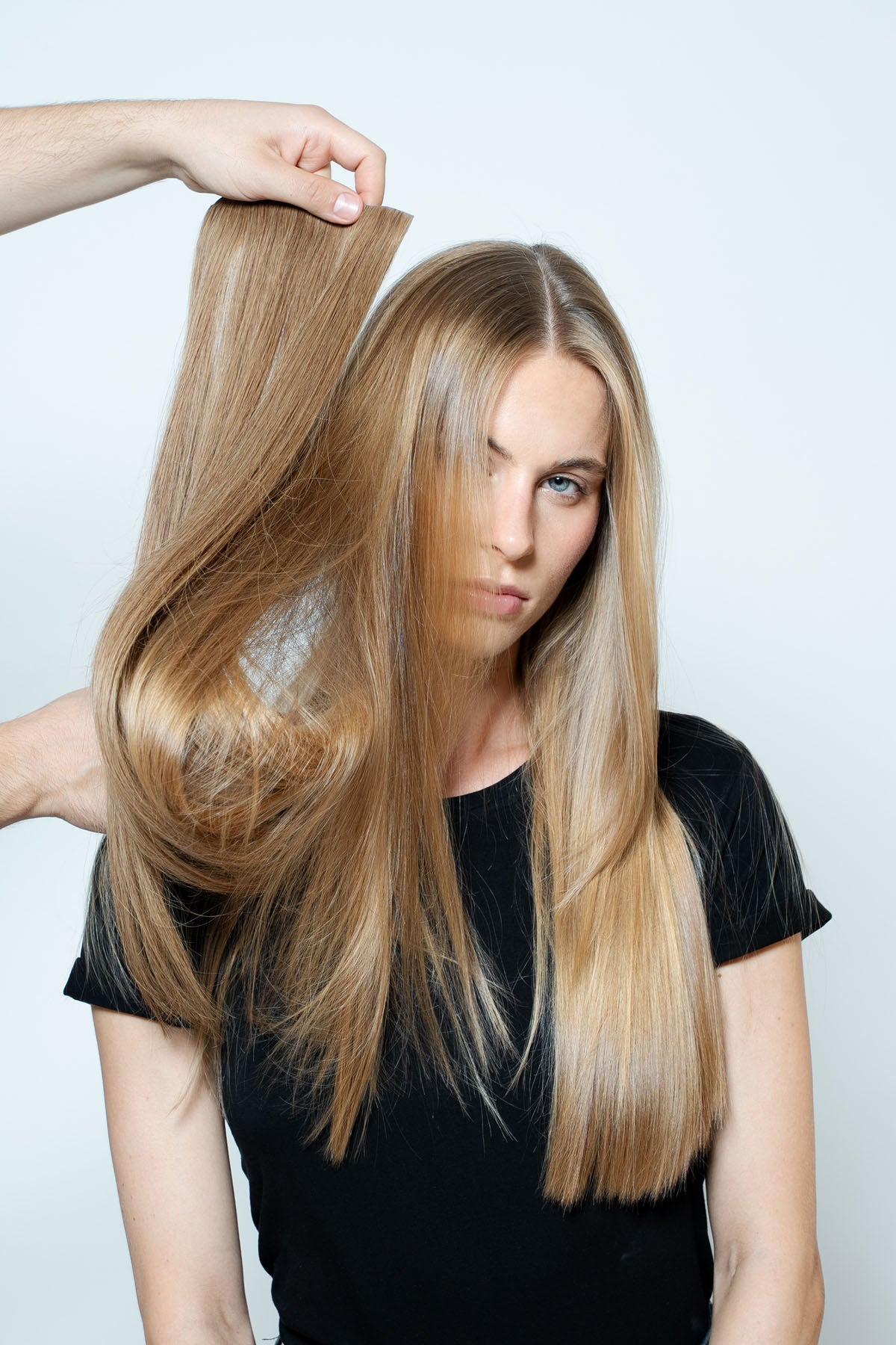 Woman holding a blonde hair extension against a plain background for 1010 Extensions