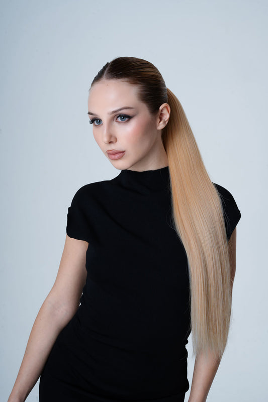 Woman with long blonde hair styled in a high ponytail by 1010 Extensions against a light gray background